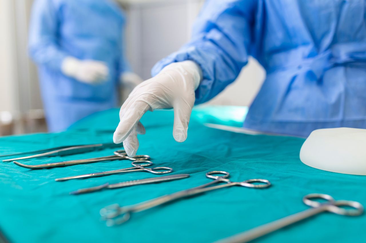 nurse hand taking surgical instrument for group of surgeons at background operating patient in surgical
